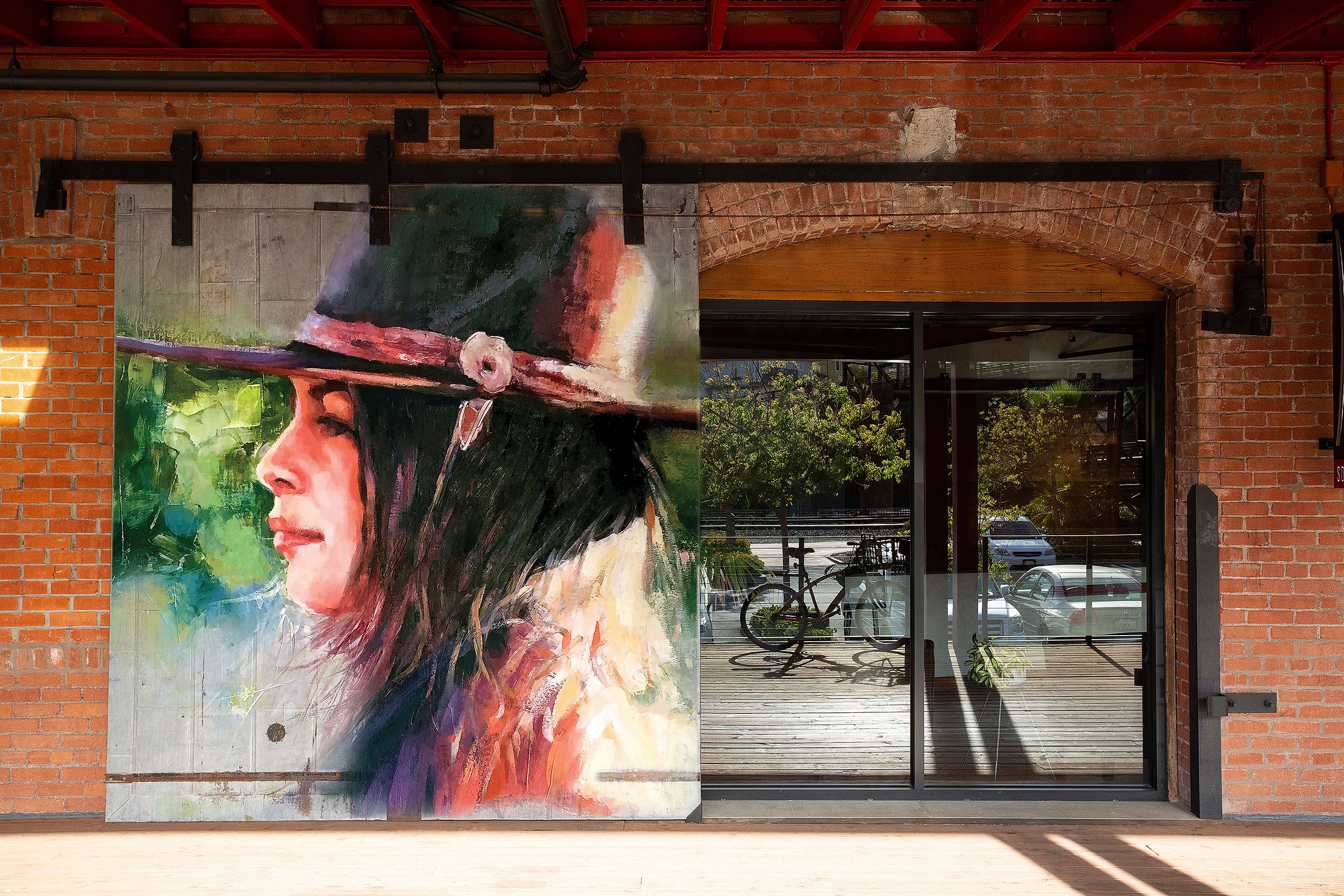 Brick building with a large mural of a woman wearing a hat on a glass door.