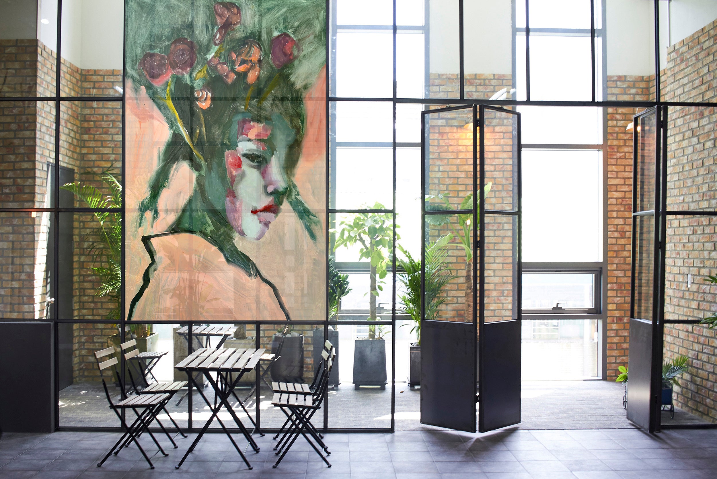 Modern commercial space with a large figurative painting, glass walls, and outdoor seating area.